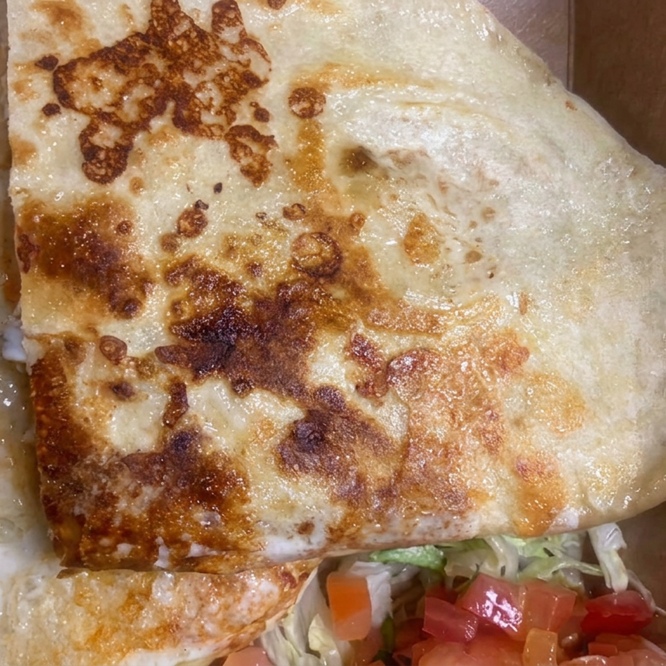 Golden-brown folded quesadilla with melted cheese, served alongside shredded lettuce, tomatoes, and red peppers.